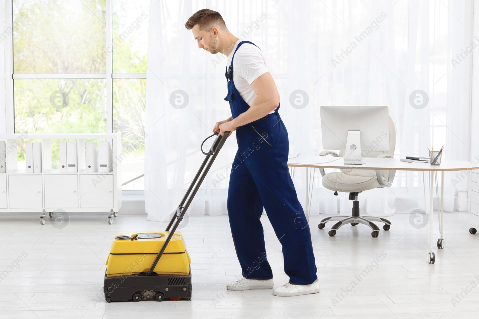 Photo of Male worker with floor cleaning machine indoors