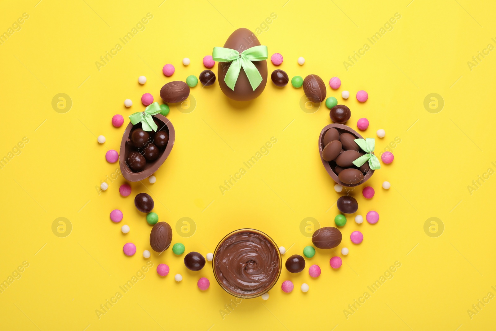 Frame made of tasty chocolate eggs with light green bows, paste and candies on yellow background, flat lay. Space for text Photo of Frame made of tasty chocolate eggs with light green bows, paste and candies on yellow background, flat lay. Space for text