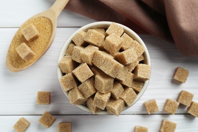 Photo of Bowl and spoon with brown sugar cubes on white wooden table, flat lay