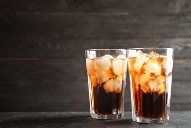 Photo of Glasses of refreshing cola with ice cubes on table. Space for text