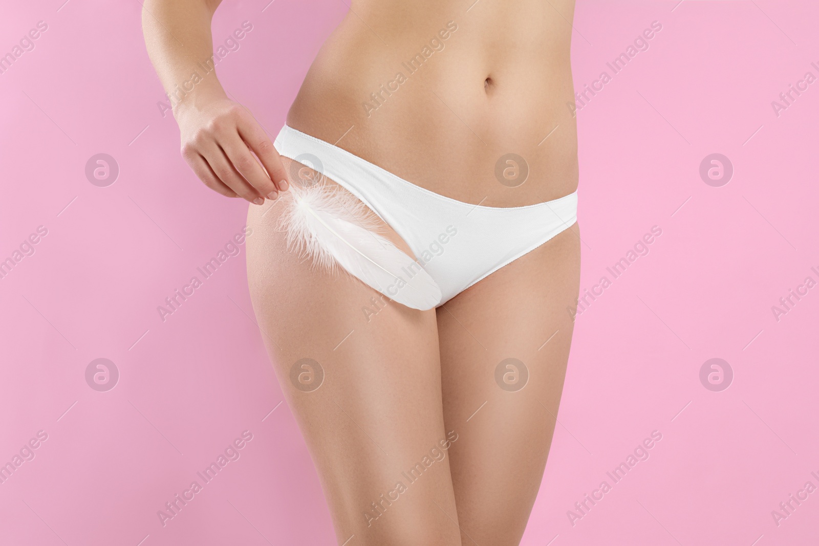 Photo of Woman with feather showing smooth skin on pink background, closeup. Brazilian bikini epilation