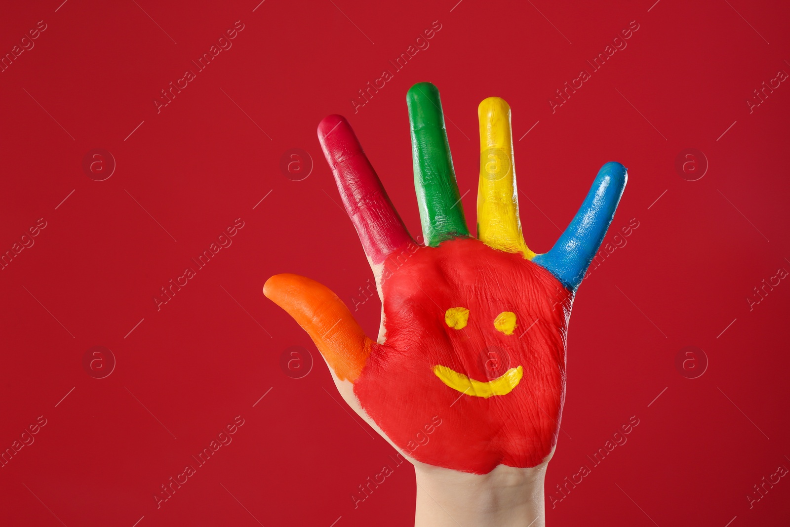 Photo of Kid with smiling face drawn on palm against red background, closeup