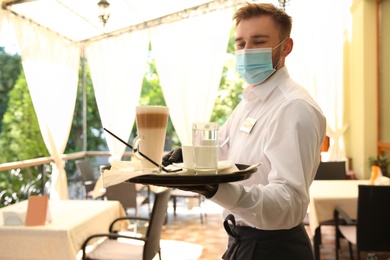 Photo of Waiter serving beverages in restaurant. Catering during coronavirus quarantine