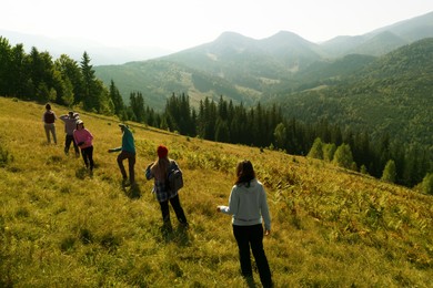 Group of tourists walking on hill in mountains, back view. Drone photography