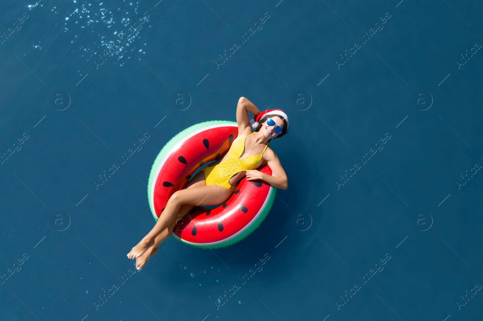 Image of Young woman wearing Santa hat and swimsuit with inflatable ring in sea, top view. Christmas vacation