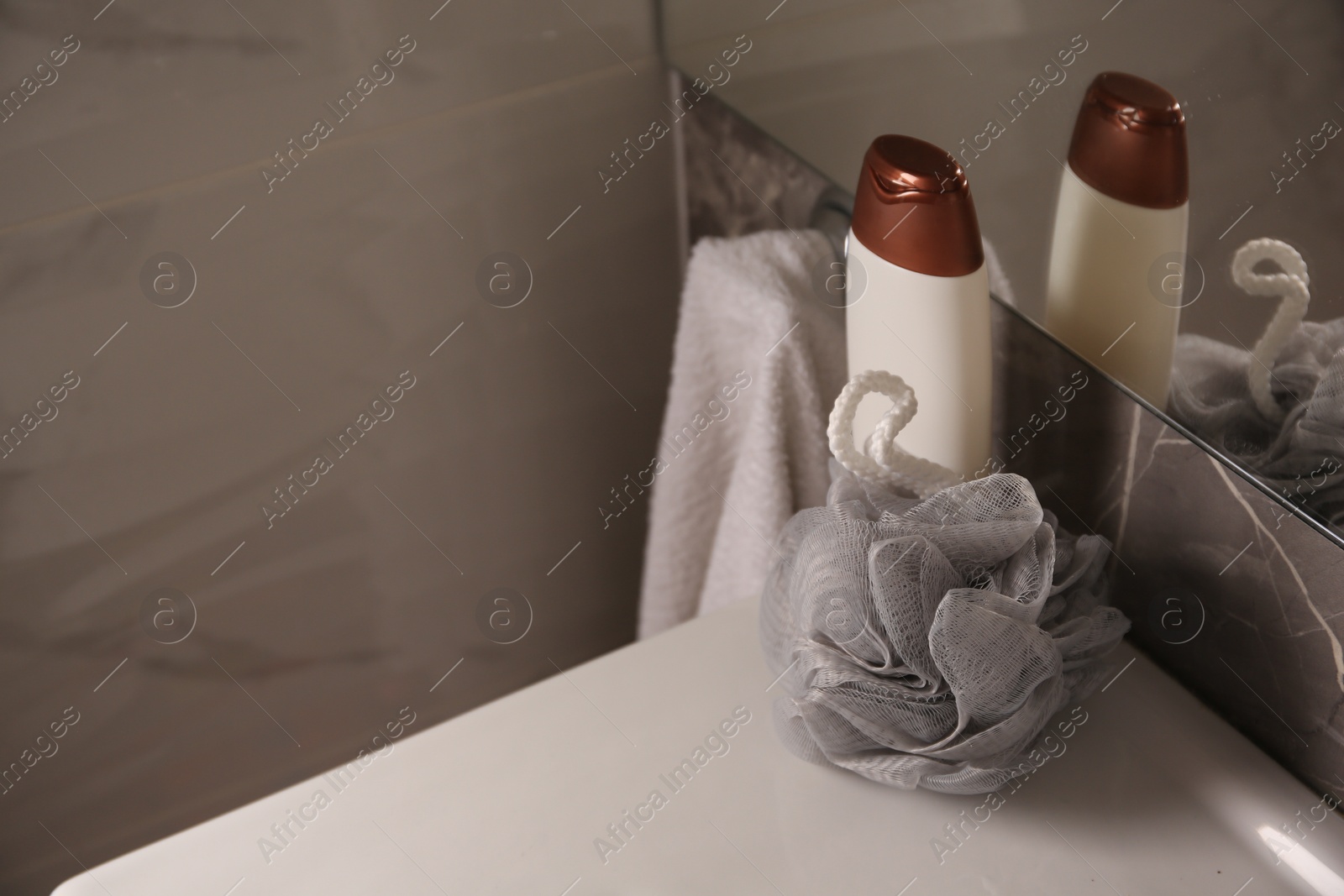 Photo of Grey sponge and shower gel bottle on washbasin in bathroom, space for text