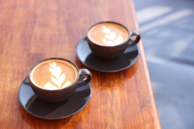 Photo of Cups of aromatic coffee with foam on wooden table in outdoor cafe. Space for text