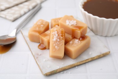 Photo of Delicious candies with sea salt and caramel sauce on white tiled table, closeup