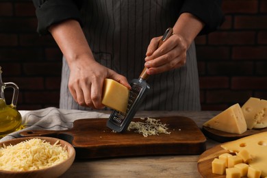 Photo of Woman grating cheese at wooden table, closeup