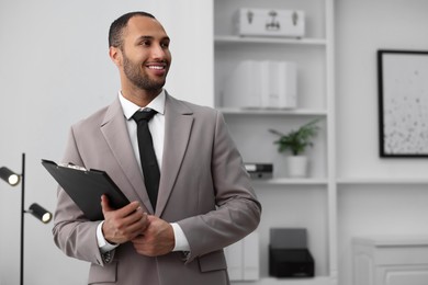 Photo of Smiling young man with clipboard in office, space for text. Lawyer, businessman, accountant or manager