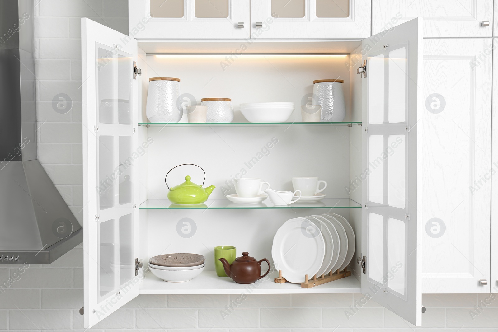 Photo of Open cabinet with different clean dishware in kitchen