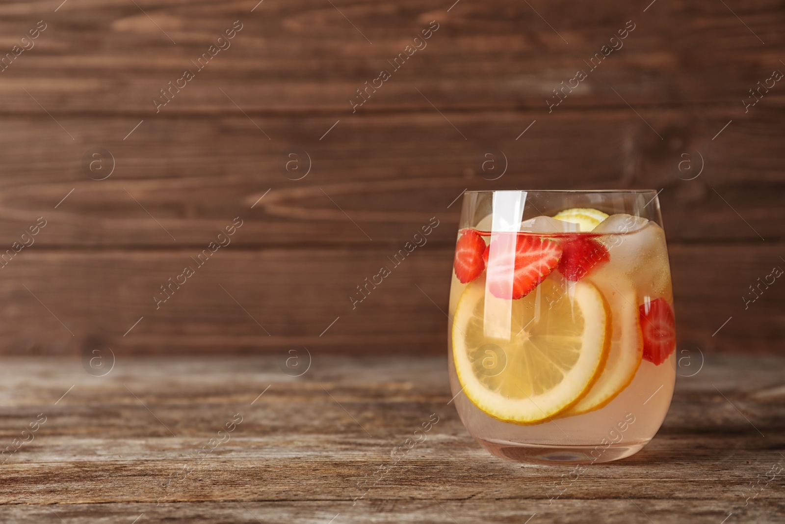 Photo of Natural lemonade with strawberries in glass on wooden table