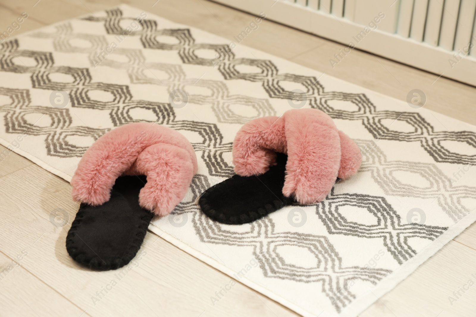 Photo of New stylish bath mat with fluffy slippers on floor indoors