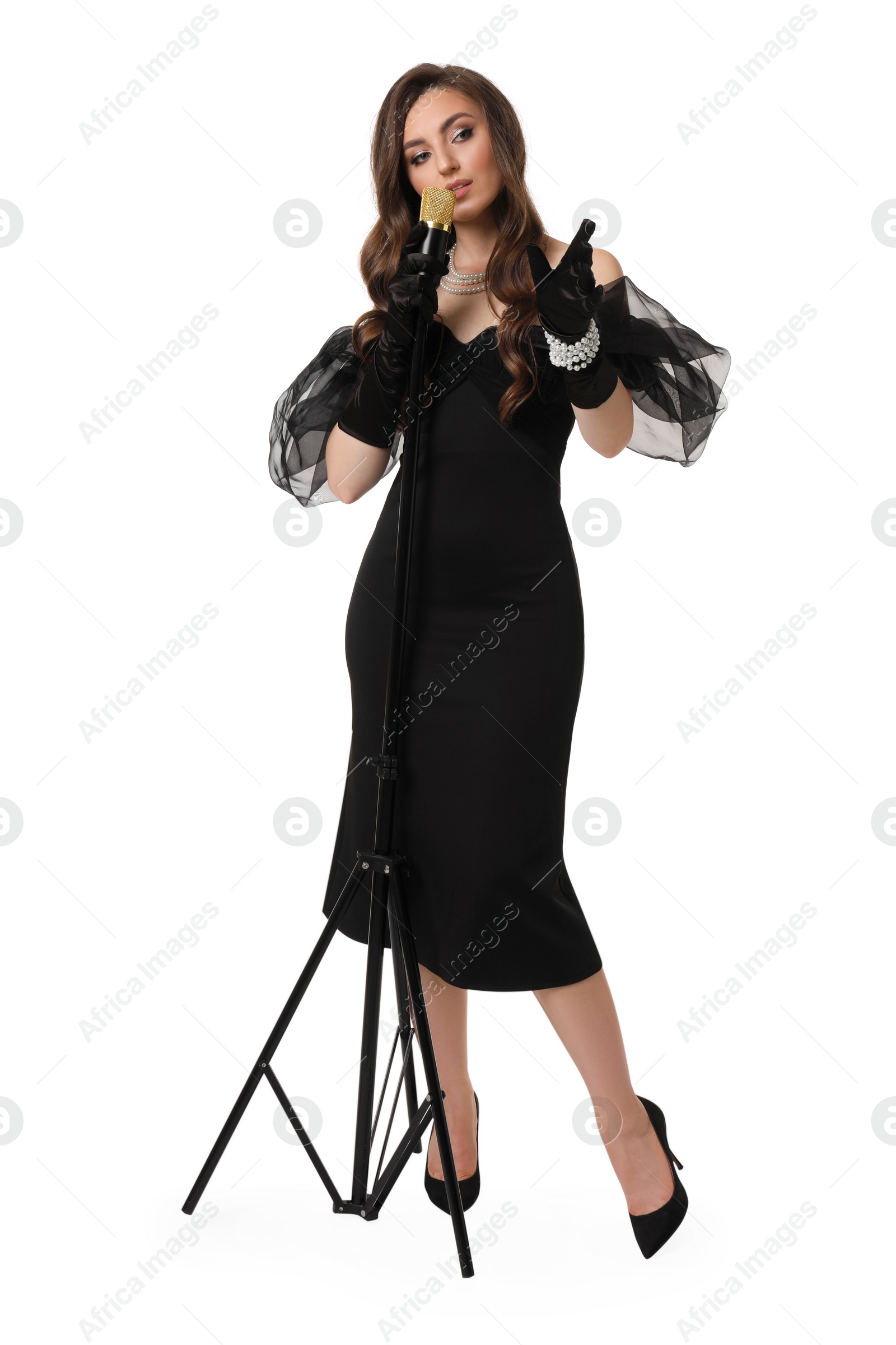 Photo of Beautiful young woman in stylish black dress with microphone singing on white background