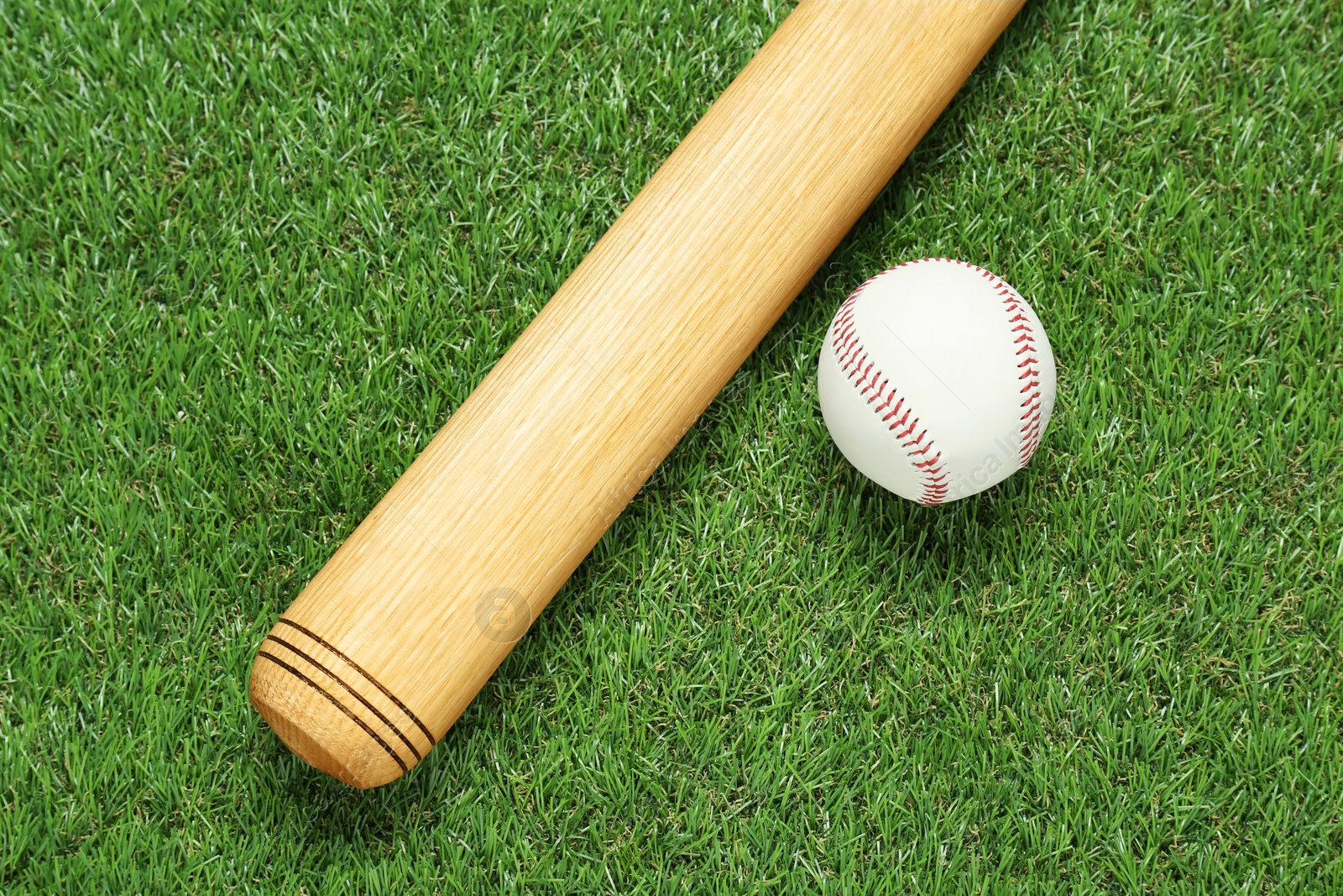 Photo of Wooden baseball bat and ball on green grass, flat lay. Sports equipment