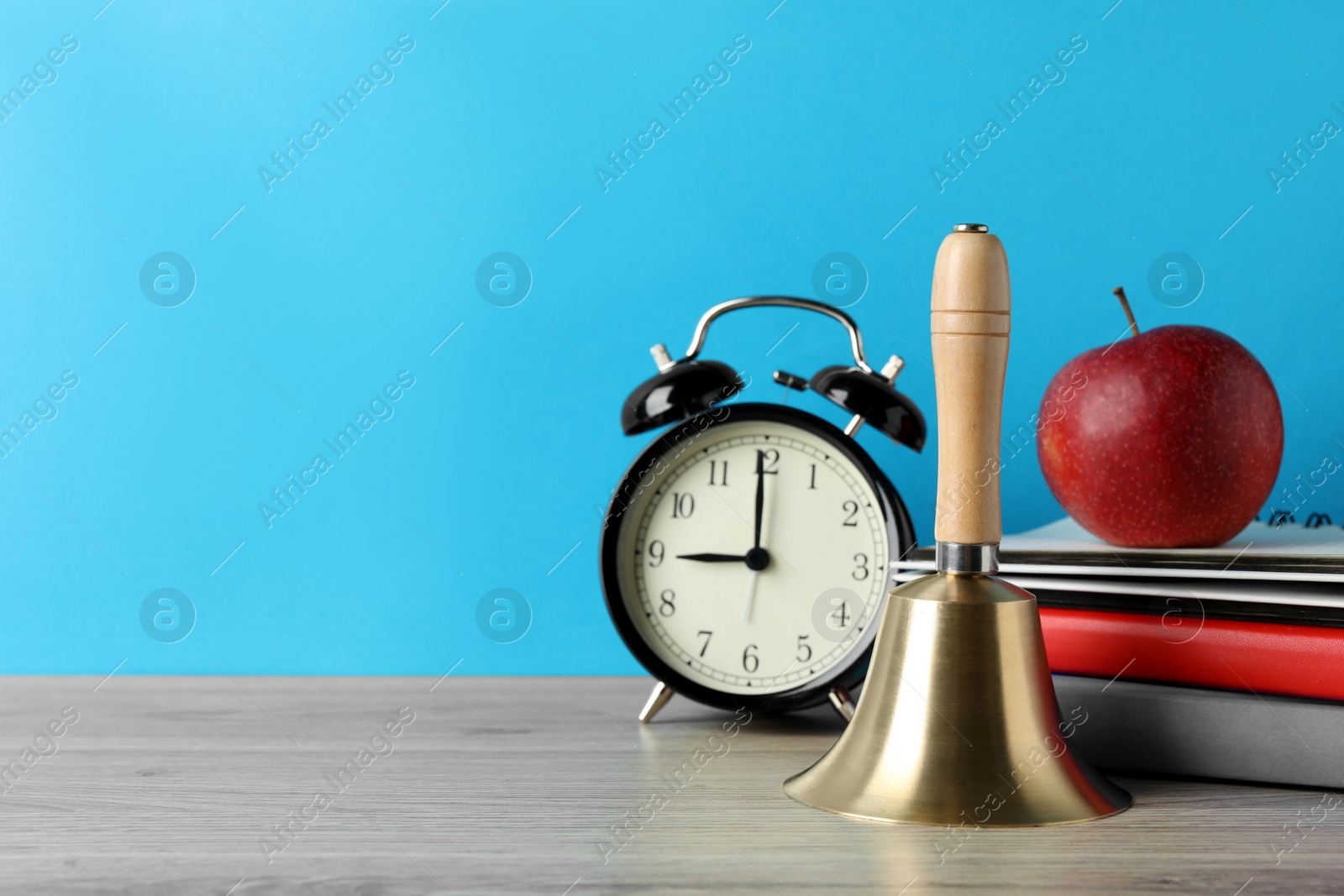 Photo of Golden school bell, apple, alarm clock and books on wooden table against turquoise background, space for text