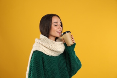 Happy beautiful woman with paper cup of mulled wine on yellow background