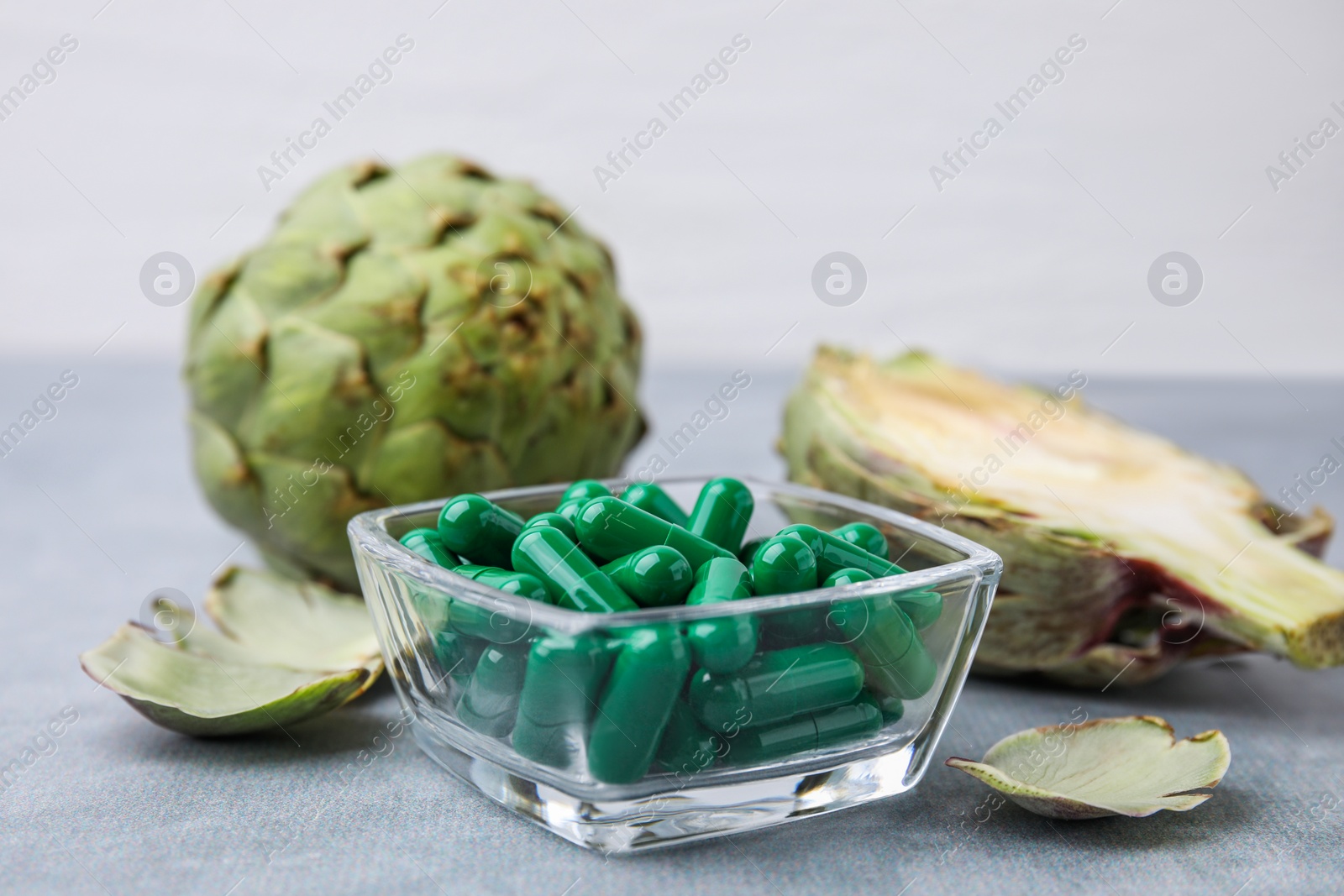 Photo of Bowl with pills and fresh artichokes on grey table, closeup