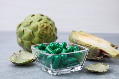 Bowl with pills and fresh artichokes on grey table, closeup