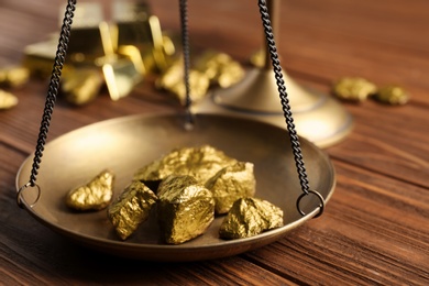 Photo of Scale pan with gold lumps on wooden table, closeup