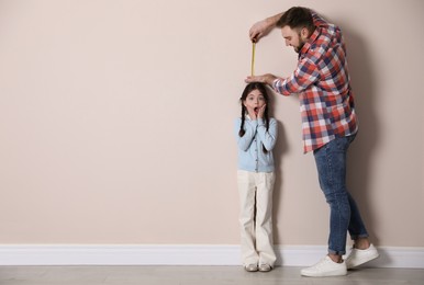 Photo of Father measuring daughter's height near beige wall indoors, space for text