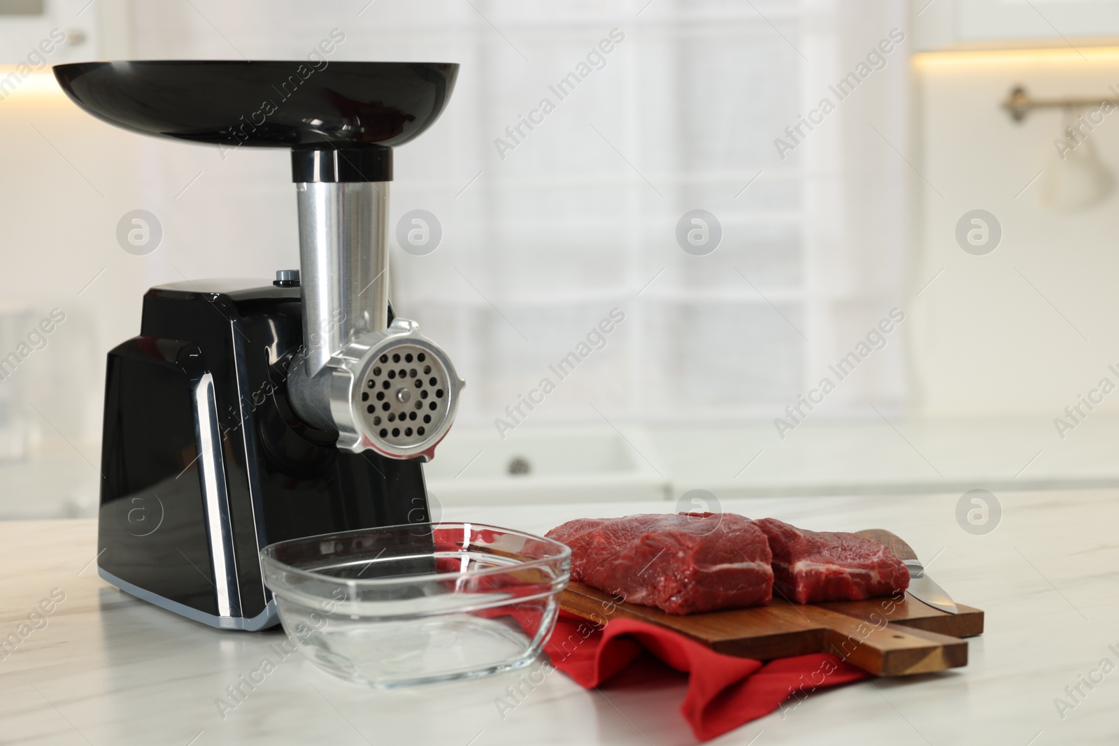 Photo of Electric meat grinder with beef on white marble table in kitchen