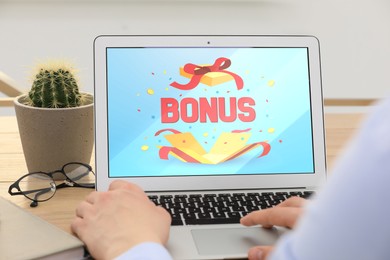 Image of Bonus gaining. Man using laptop at table, closeup. Illustration of open gift box, word and confetti on device screen
