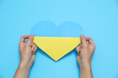 Photo of Man holding paper heart in colors of Ukrainian flag on light blue background, top view