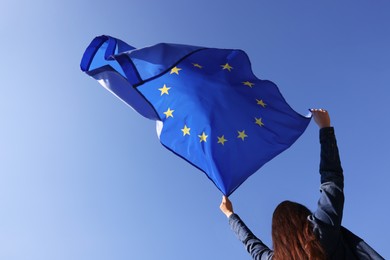 Photo of Woman holding European Union flag against blue sky outdoors, low angle view