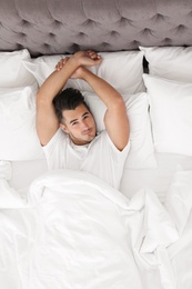 Young man lying in bed with soft pillows at home, top view