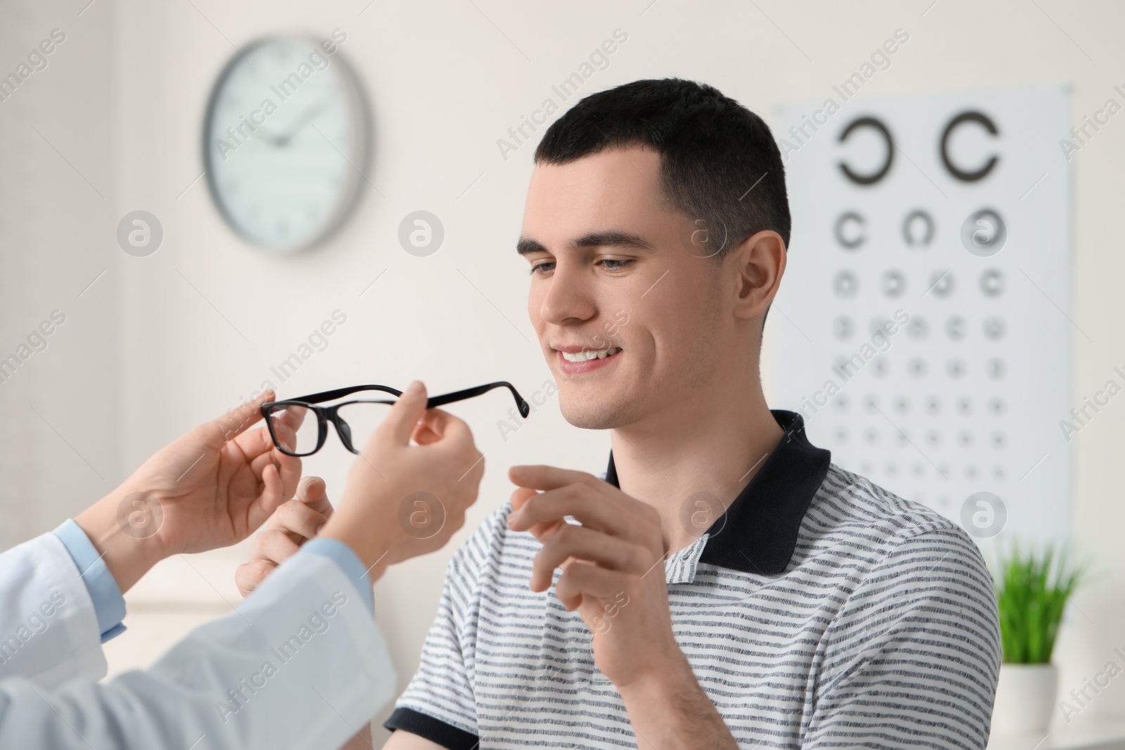 Photo of Vision testing. Ophthalmologist giving glasses to young man indoors