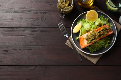 Delicious cooked salmon with pesto sauce, lettuce and lemon on wooden table, flat lay. Space for text