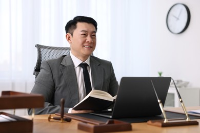 Happy notary working with laptop and book at wooden table in office