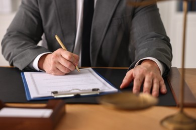 Photo of Notary writing notes at wooden table in office, closeup