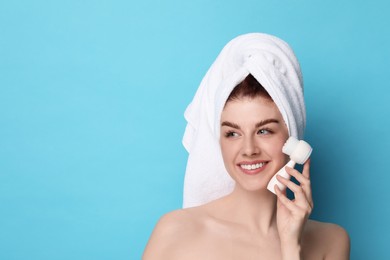 Washing face. Young woman with cleansing brush on light blue background, space for text