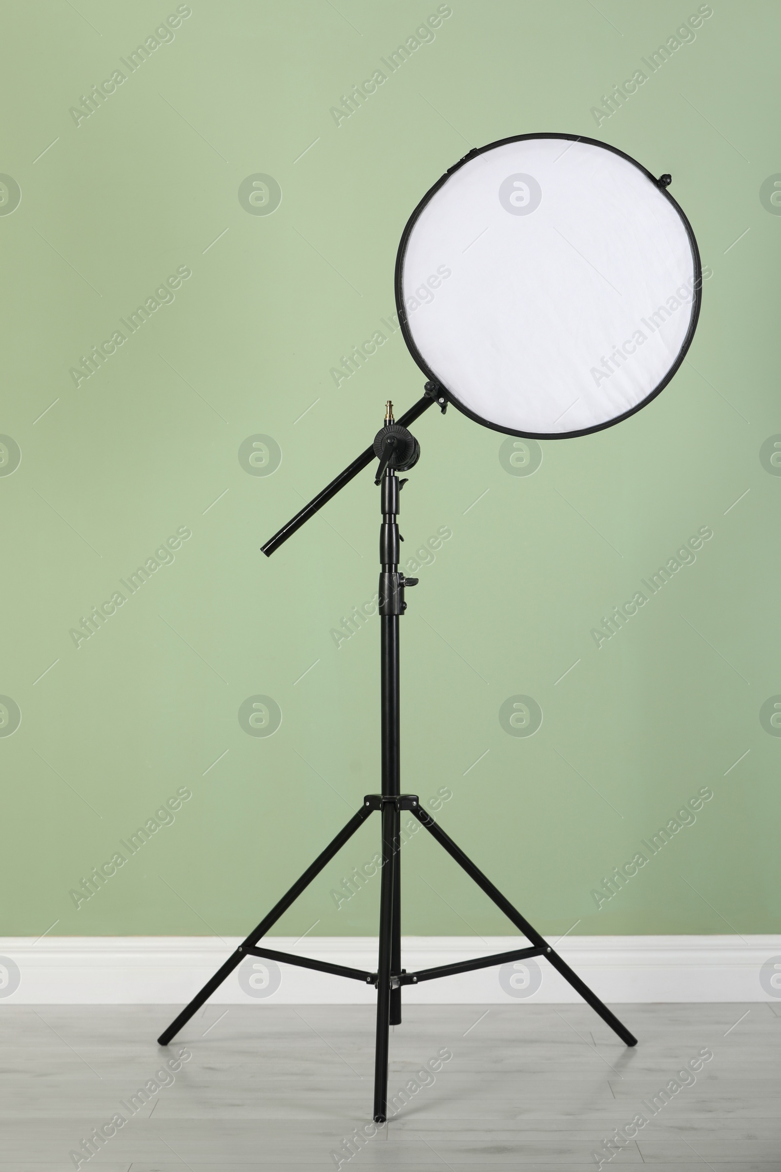 Photo of Studio reflector on tripod near pale green wall indoors. Professional photographer's equipment