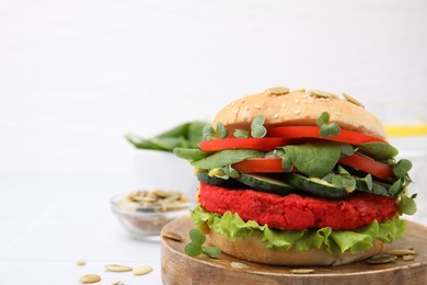 Photo of Tasty vegan burger with vegetables, patty and microgreens on white tiled table, closeup. Space for text