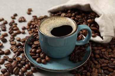 Cup of aromatic hot coffee and beans on light grey table