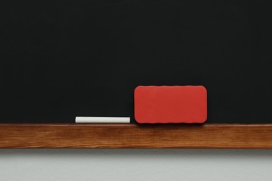 Clean blackboard with chalk and duster hanging on grey wall