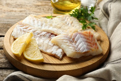 Photo of Fresh raw cod fillets, parsley and lemon on wooden table, closeup