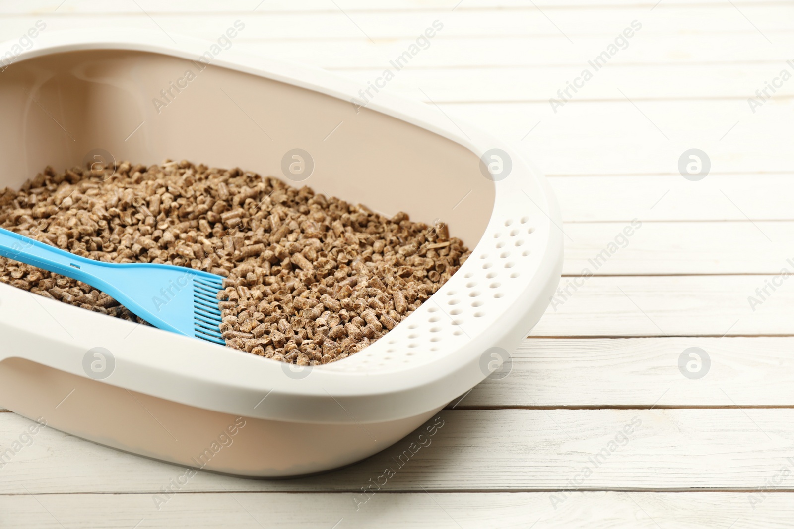 Photo of Cat litter tray with filler and scoop on white wooden floor, closeup