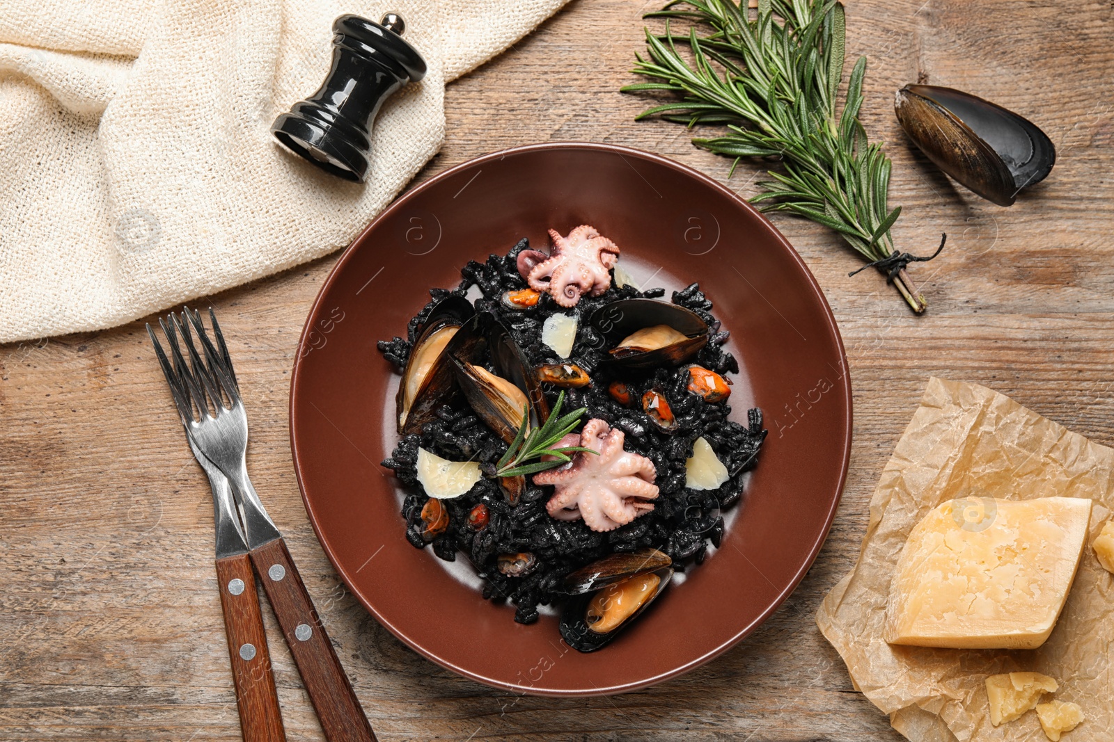Photo of Delicious black risotto with seafood served on wooden table, flat lay