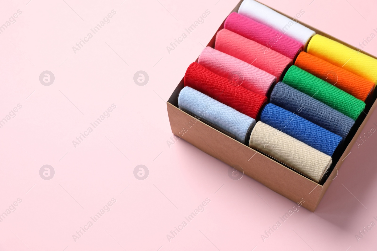 Photo of Box with different colorful socks on light pink background. Space for text