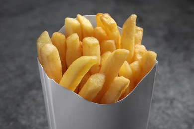 Photo of Delicious french fries in paper box on light grey background, closeup