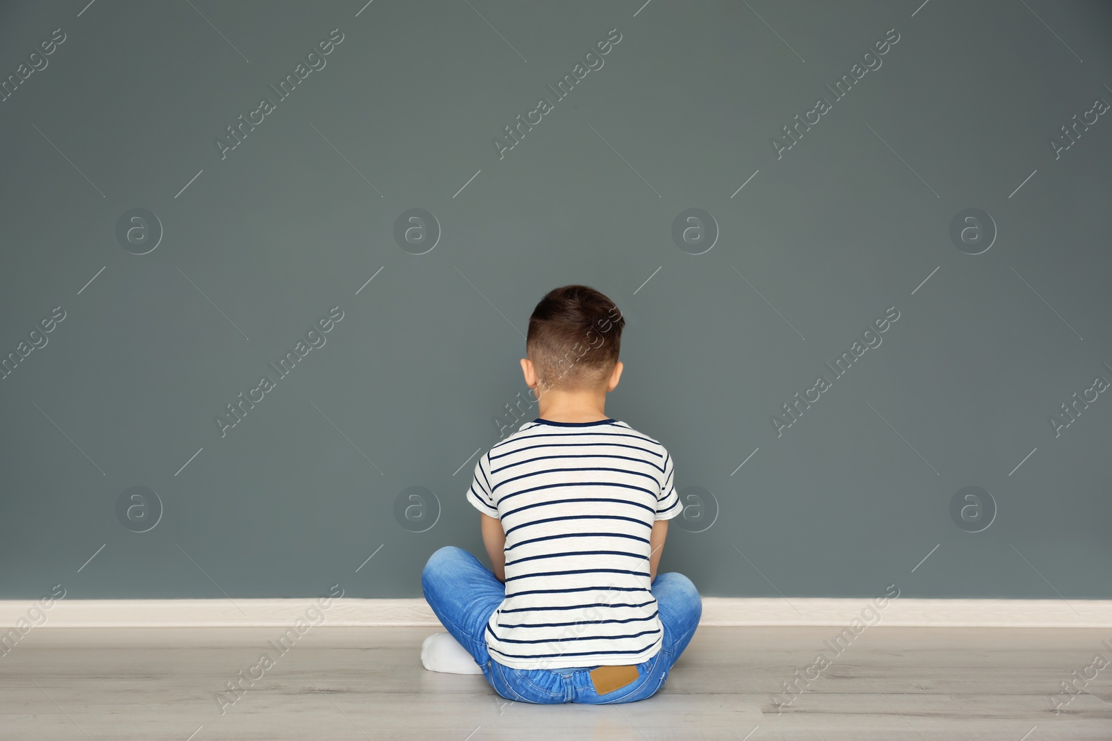 Photo of Lonely little boy sitting on floor in room. Autism concept