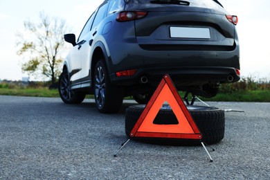 Emergency warning triangle and tire near car on roadside