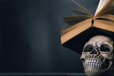 Human skull and old book against black background. Space for text