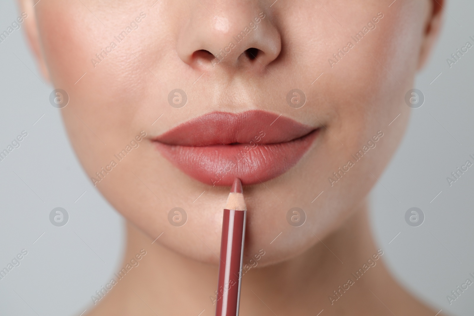 Photo of Young woman applying beautiful nude lip pencil on light grey background, closeup