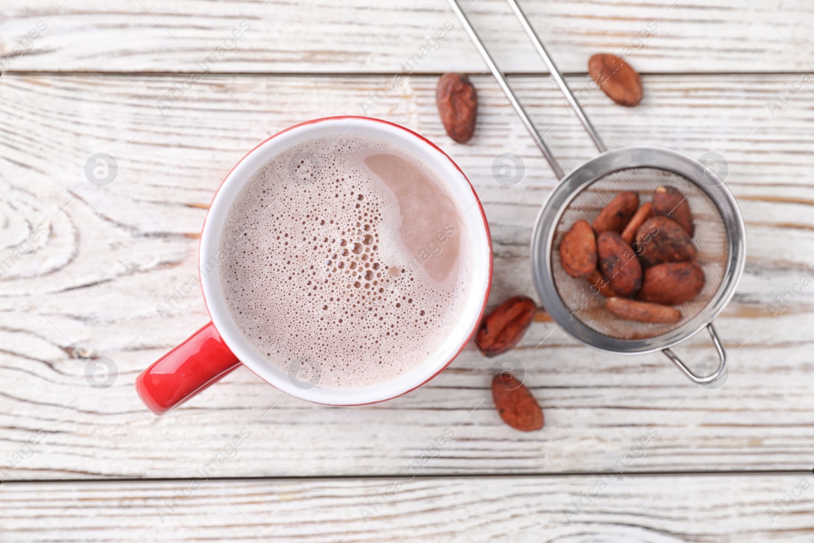 Photo of Cup of tasty cocoa and beans on white wooden table, flat lay