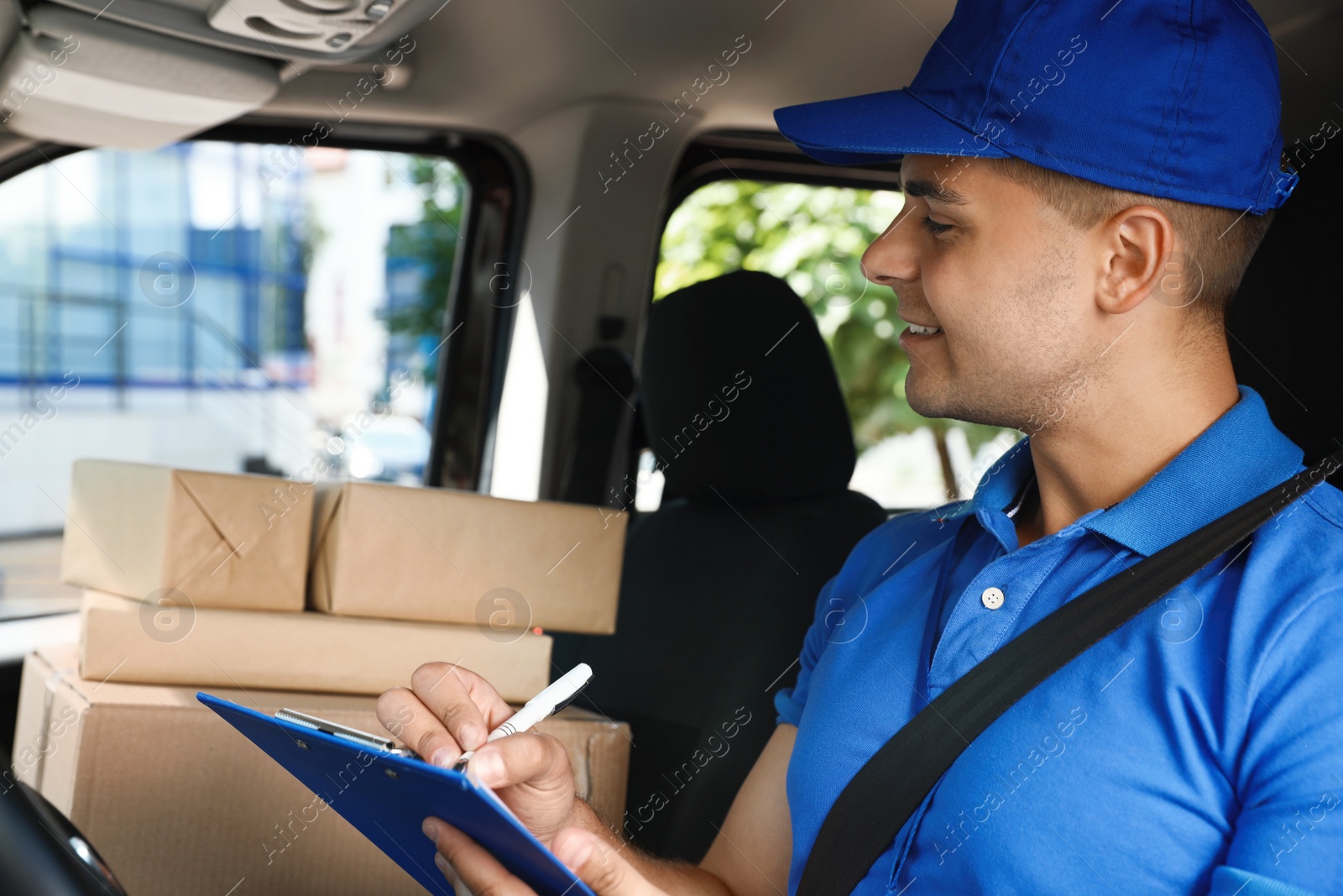 Photo of Young courier with parcels and clipboard in delivery car